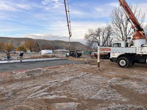 Construction site with a white crane truck lifting a cable over a muddy lot at dusk