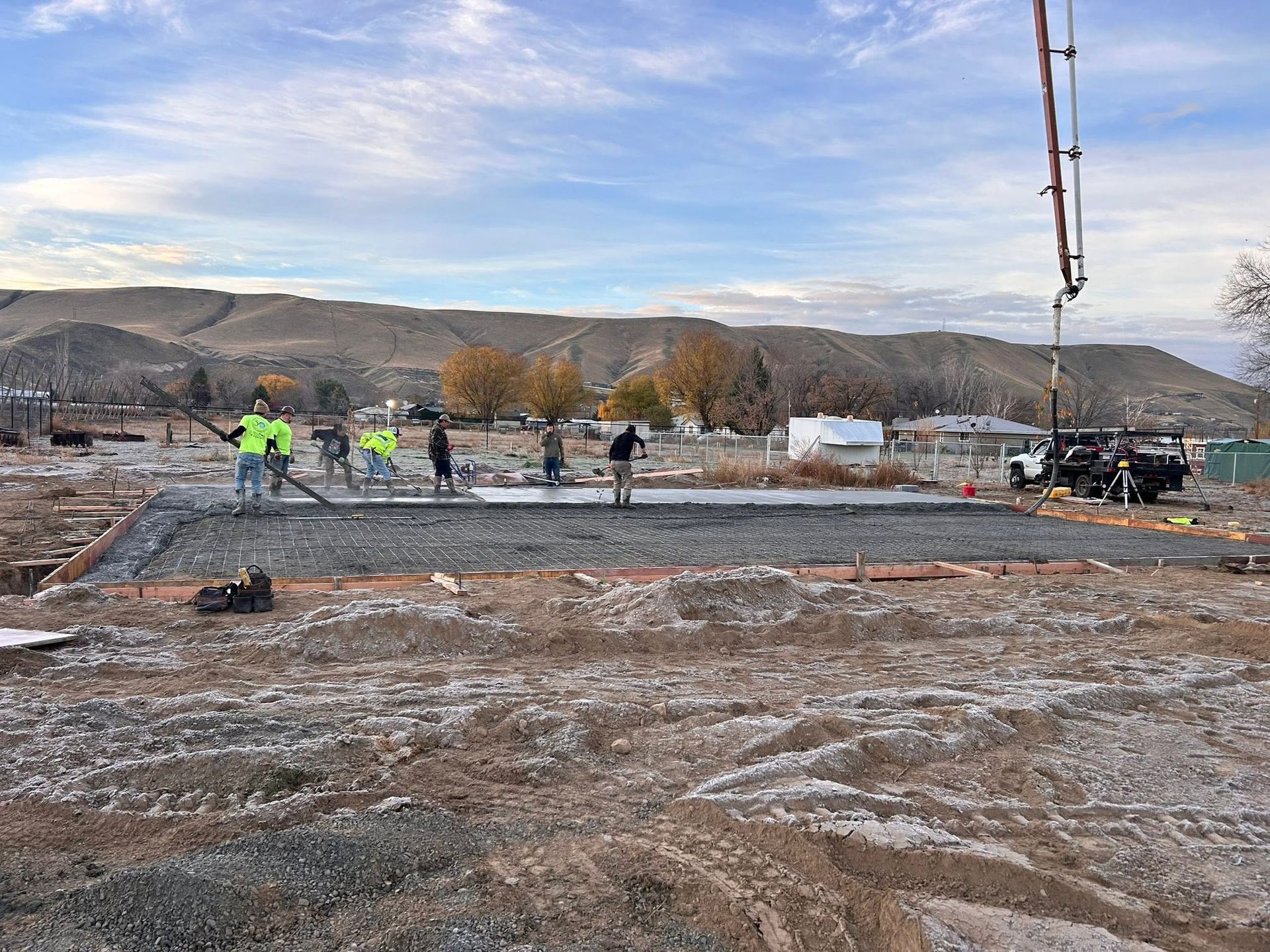 Construction crew pouring concrete at a worksite with mountains in the background.