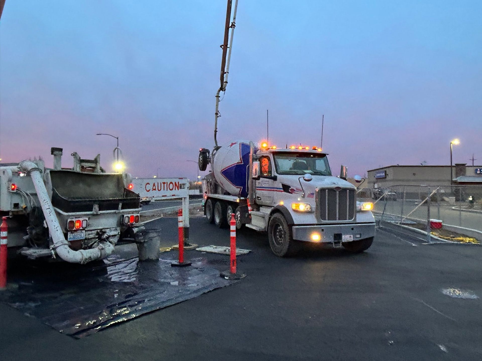 Tow truck and flatbed on a wet road at dusk with safety cones and flashing lights