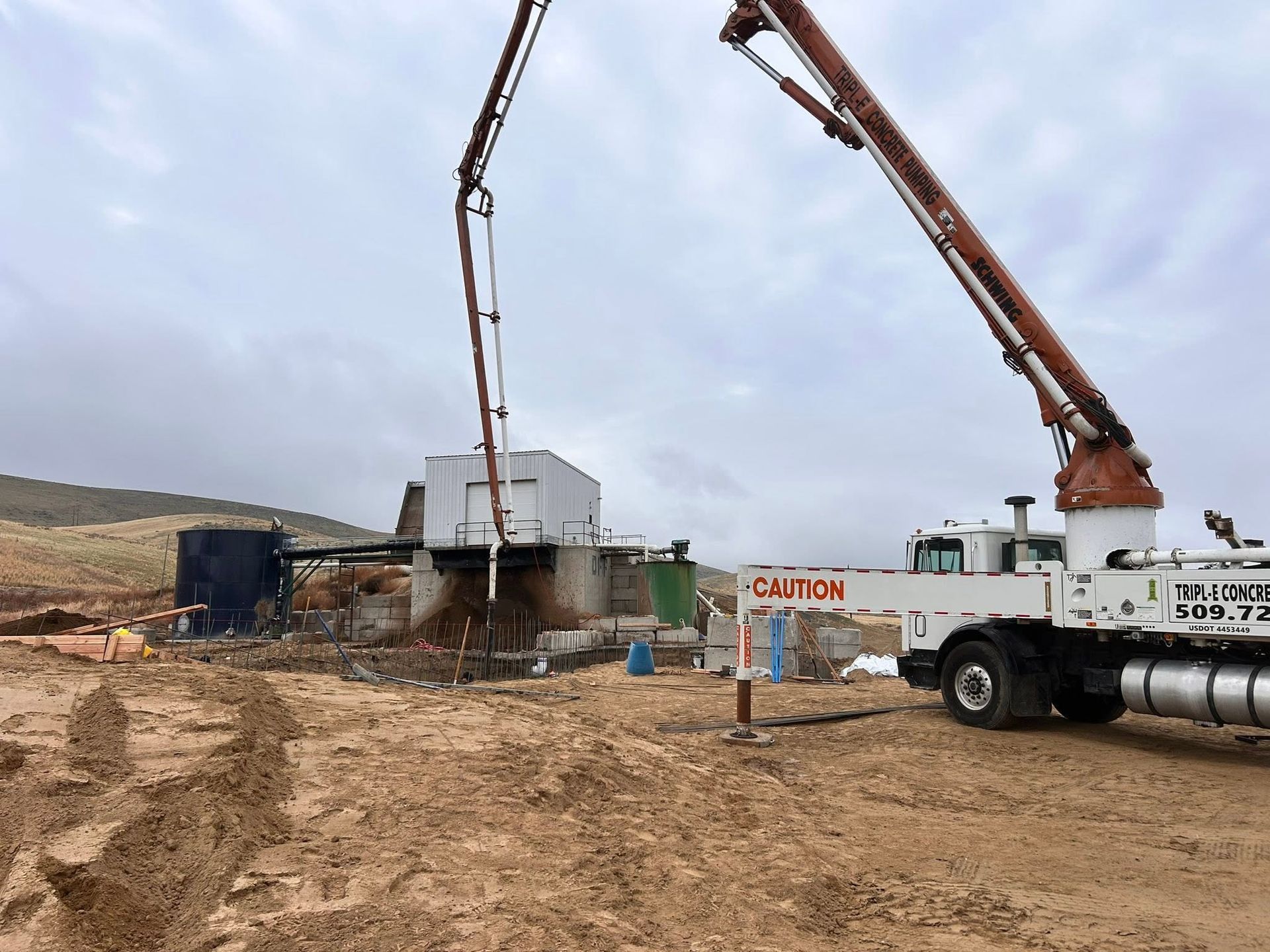 Concrete pump truck pouring concrete at a muddy construction site under overcast skies
