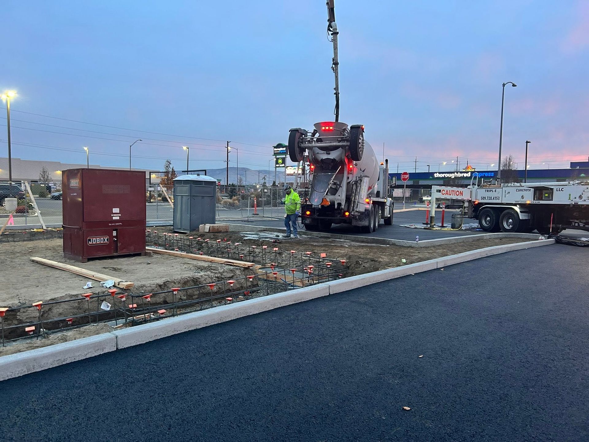 Construction truck at dusk near a curb, with workers and equipment on a paved roadside.