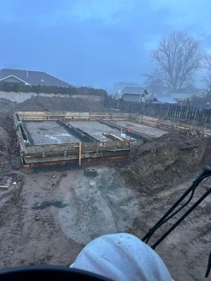 Construction site with foundation forms in muddy ground under a cloudy blue sky