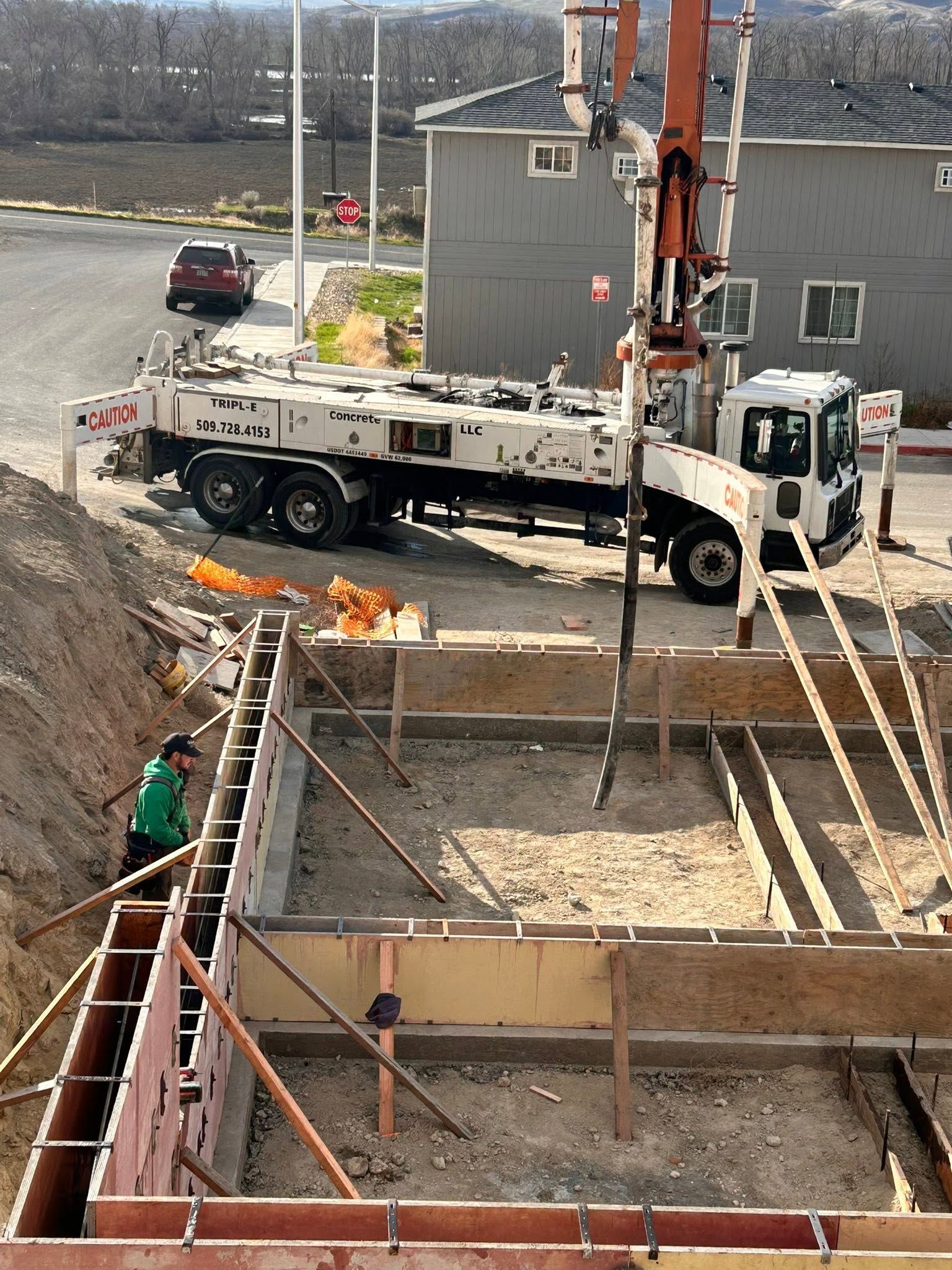 Construction site with a crane truck lifting materials beside a concrete foundation and ladders