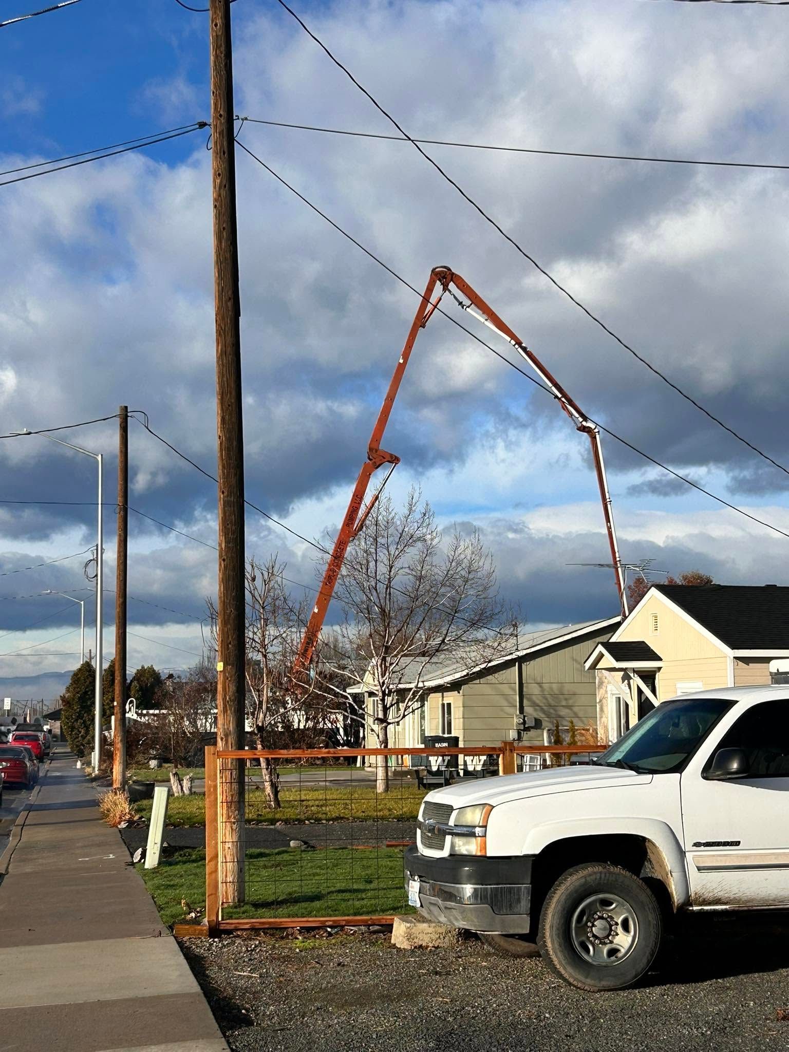 Broken wooden utility pole leaning over a residential street beside a white pickup truck and sidewalk.