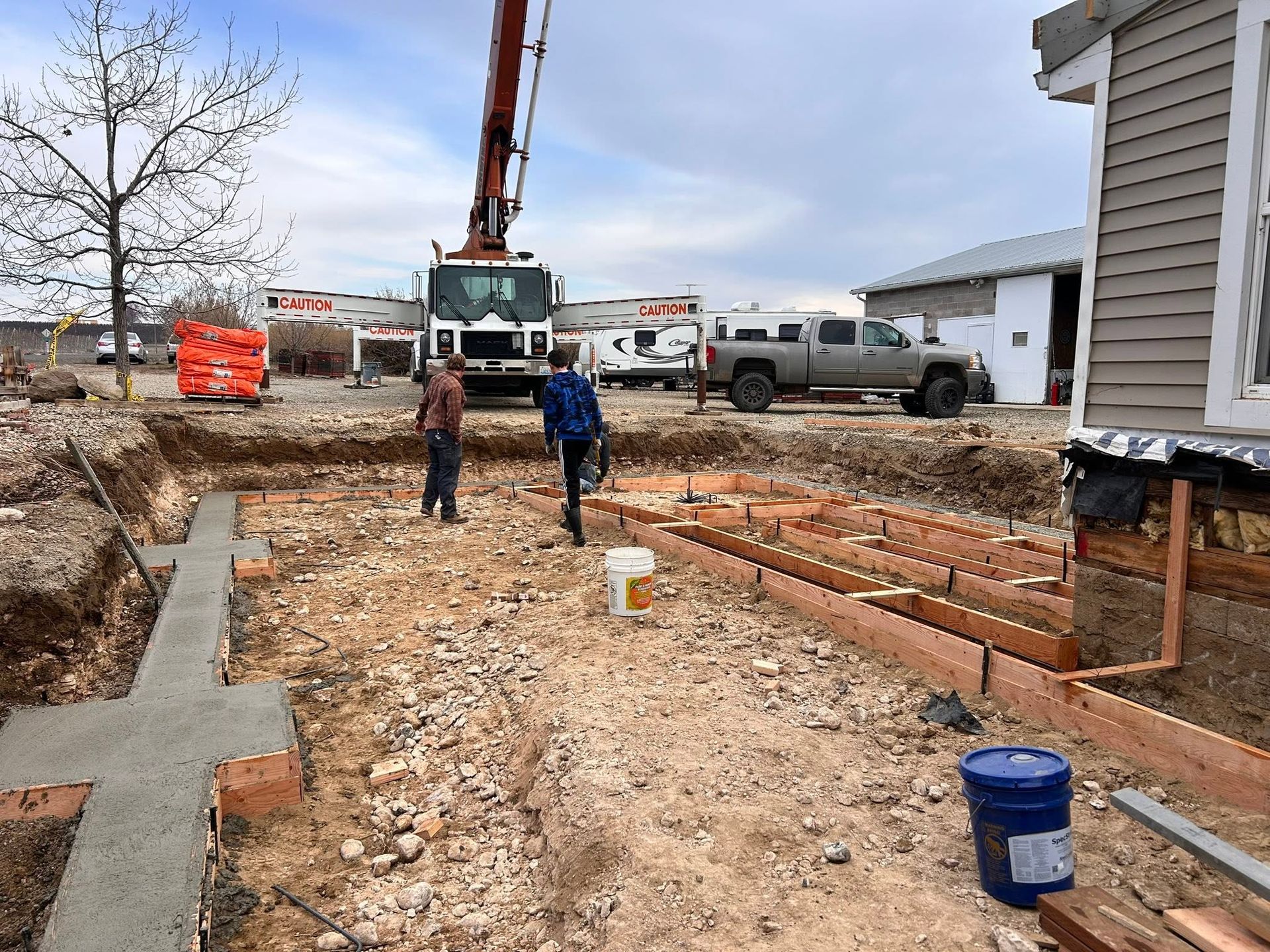Construction site with two workers, concrete forms, and a crane near a house.