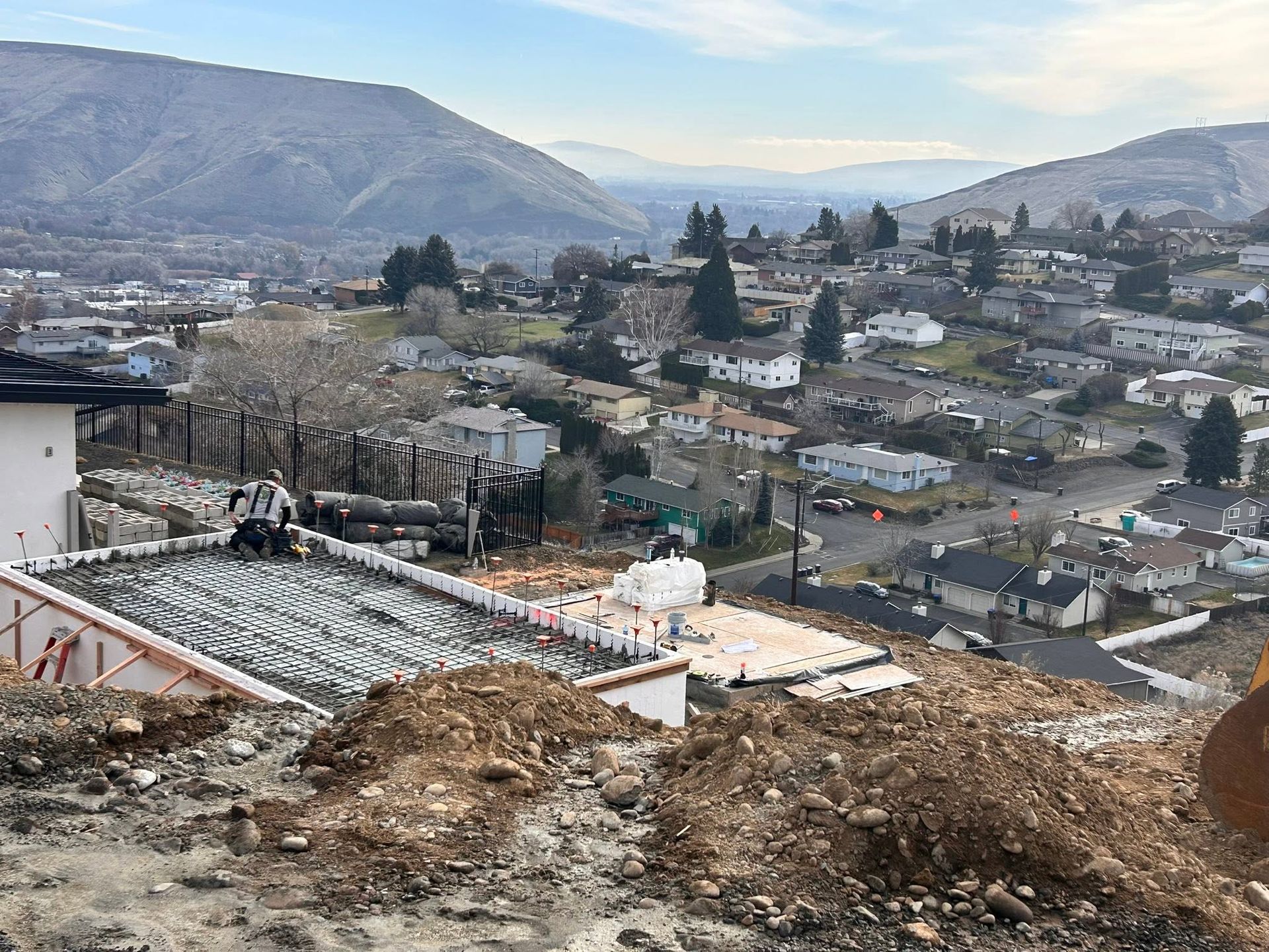 Aerial view of a hillside neighborhood with scattered houses, roads, and mountains in the background.