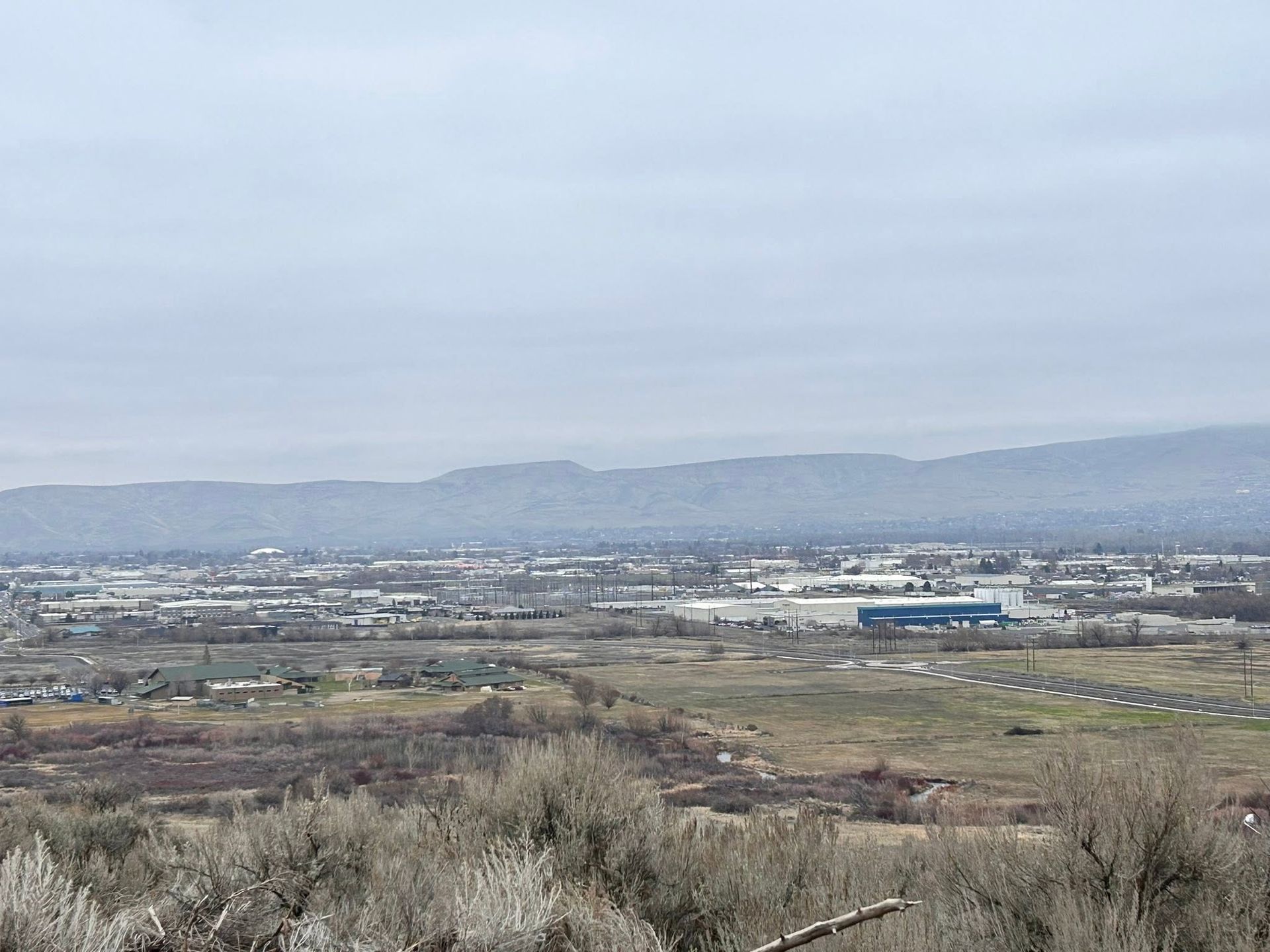 Wide view of a cloudy valley with fields, scattered buildings, and distant mountains.