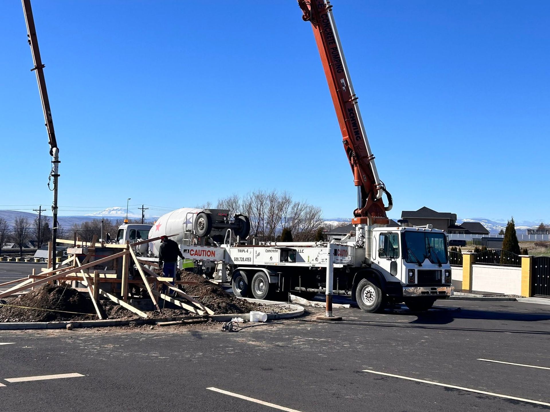 Construction vehicle and red crane at a debris-filled roadside worksite under a clear blue sky
