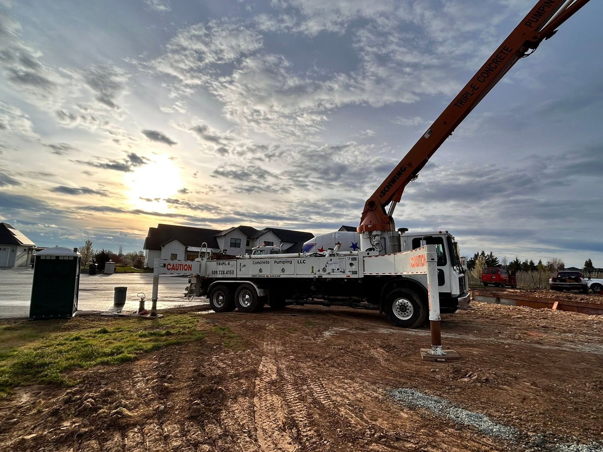 Concrete truck with extended boom at a construction site at sunset under a cloudy sky