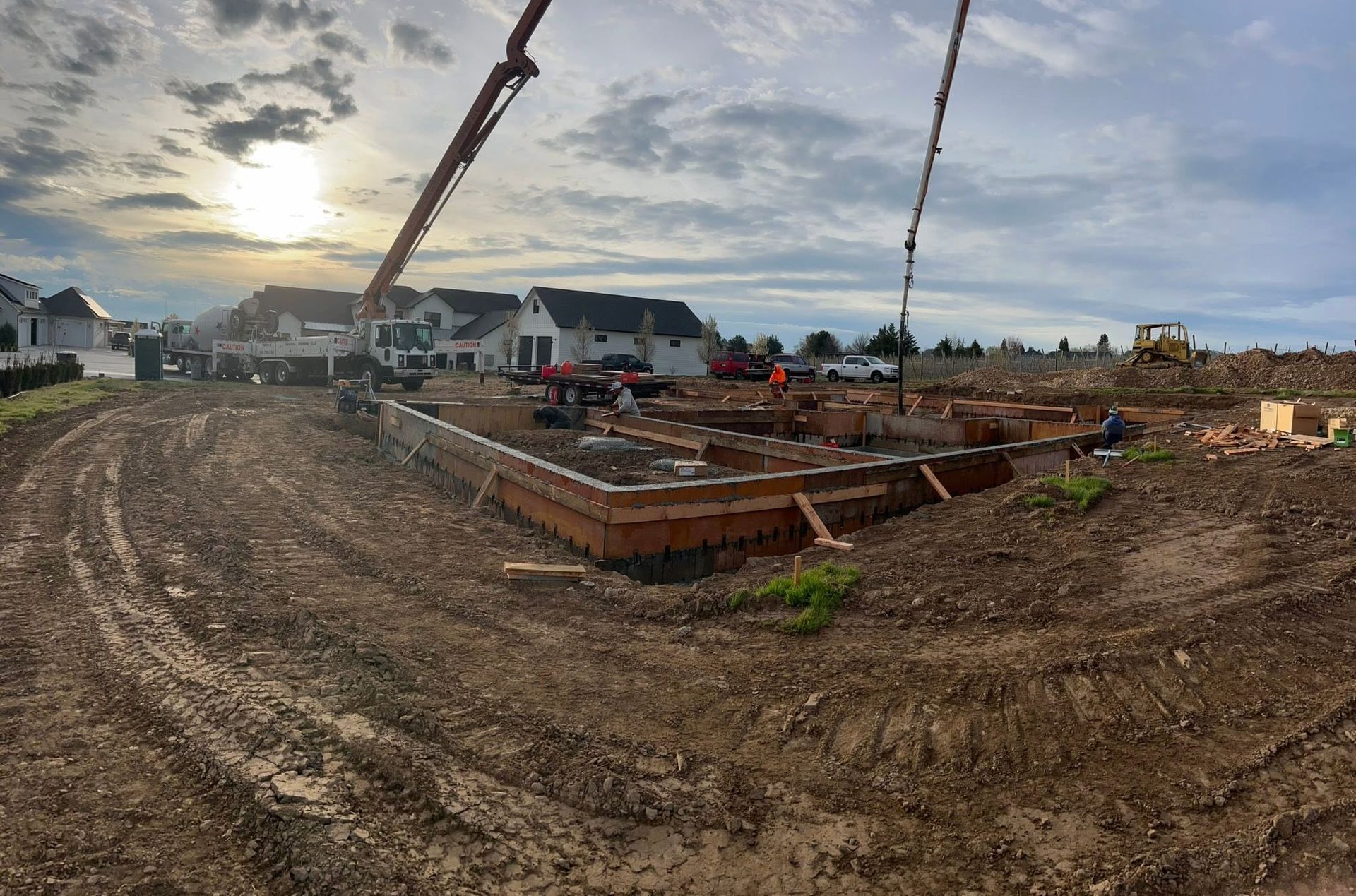 Construction site with foundation forms and a concrete pump under a cloudy sky at sunrise