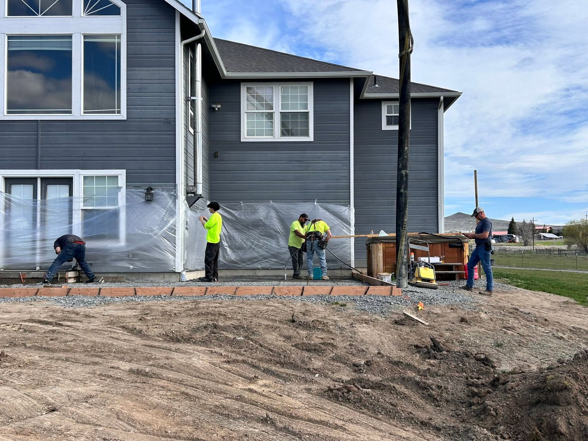 Workers laying concrete beside a gray house on a construction site