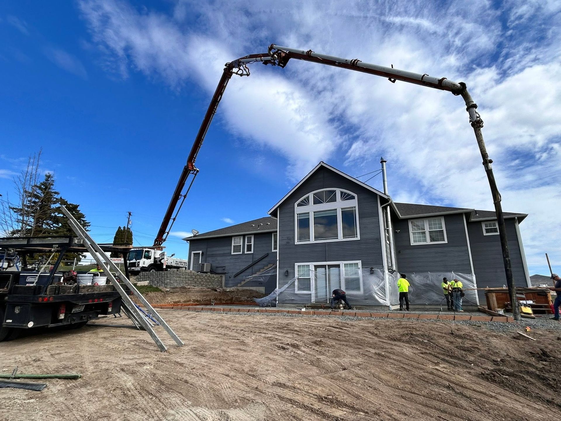 A crane lifts a large gray house frame at a construction site under a blue sky.