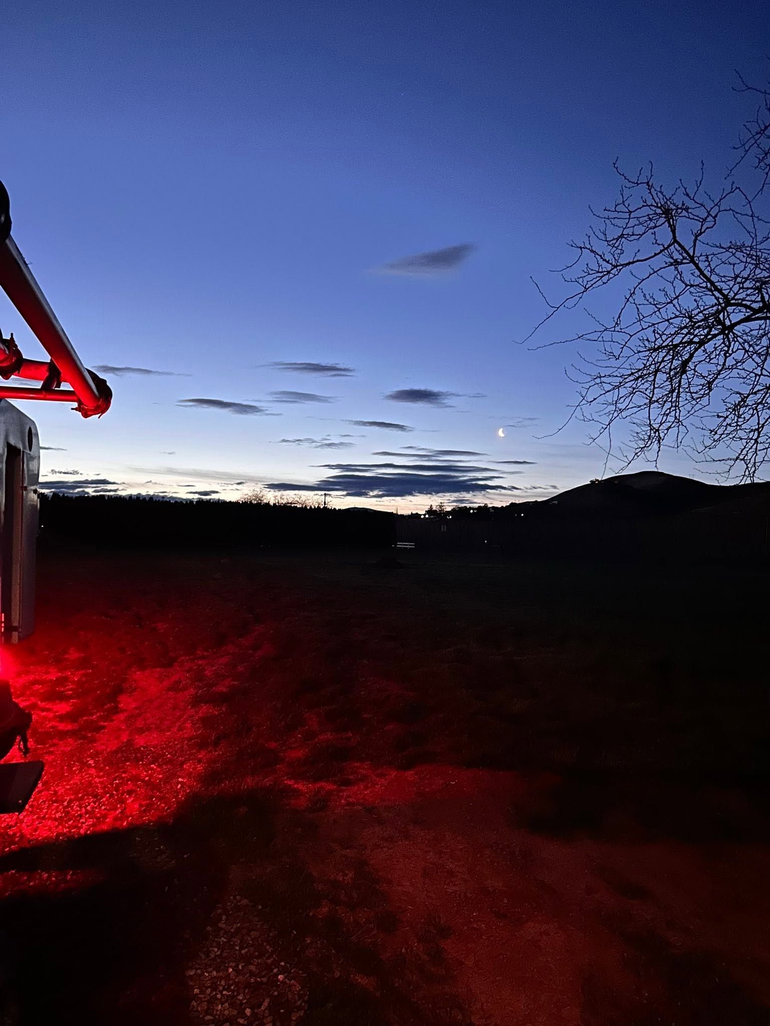 Dusk sky over a dark field, with red light illuminating the ground and a silhouetted tree on the right.