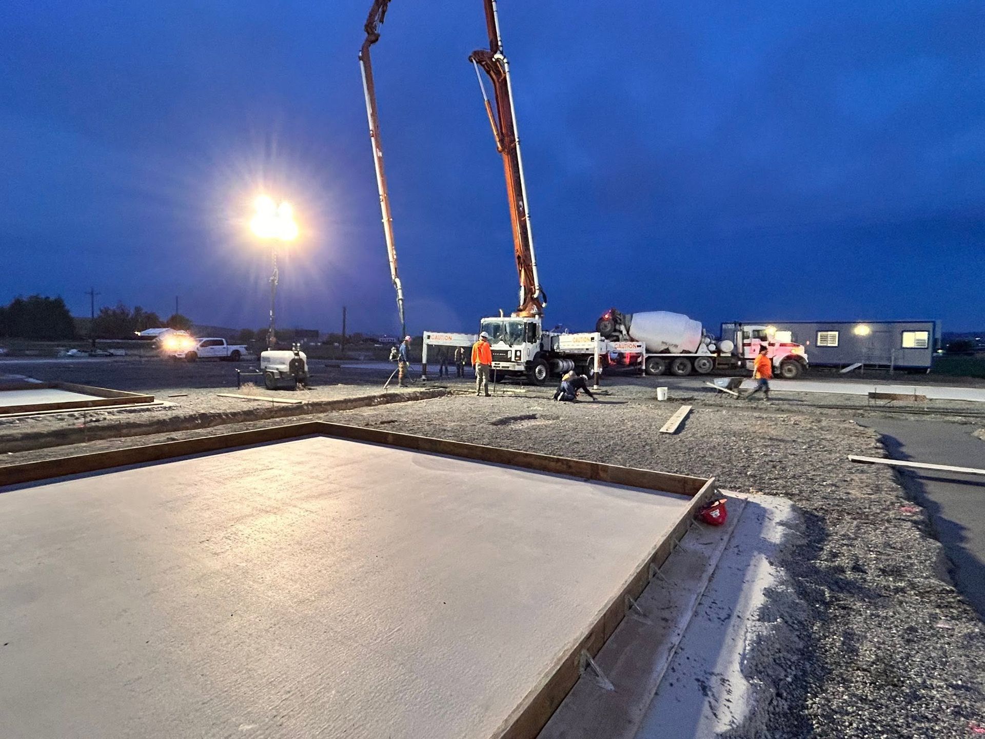 Concrete slab being poured at dusk by a crane on a construction site