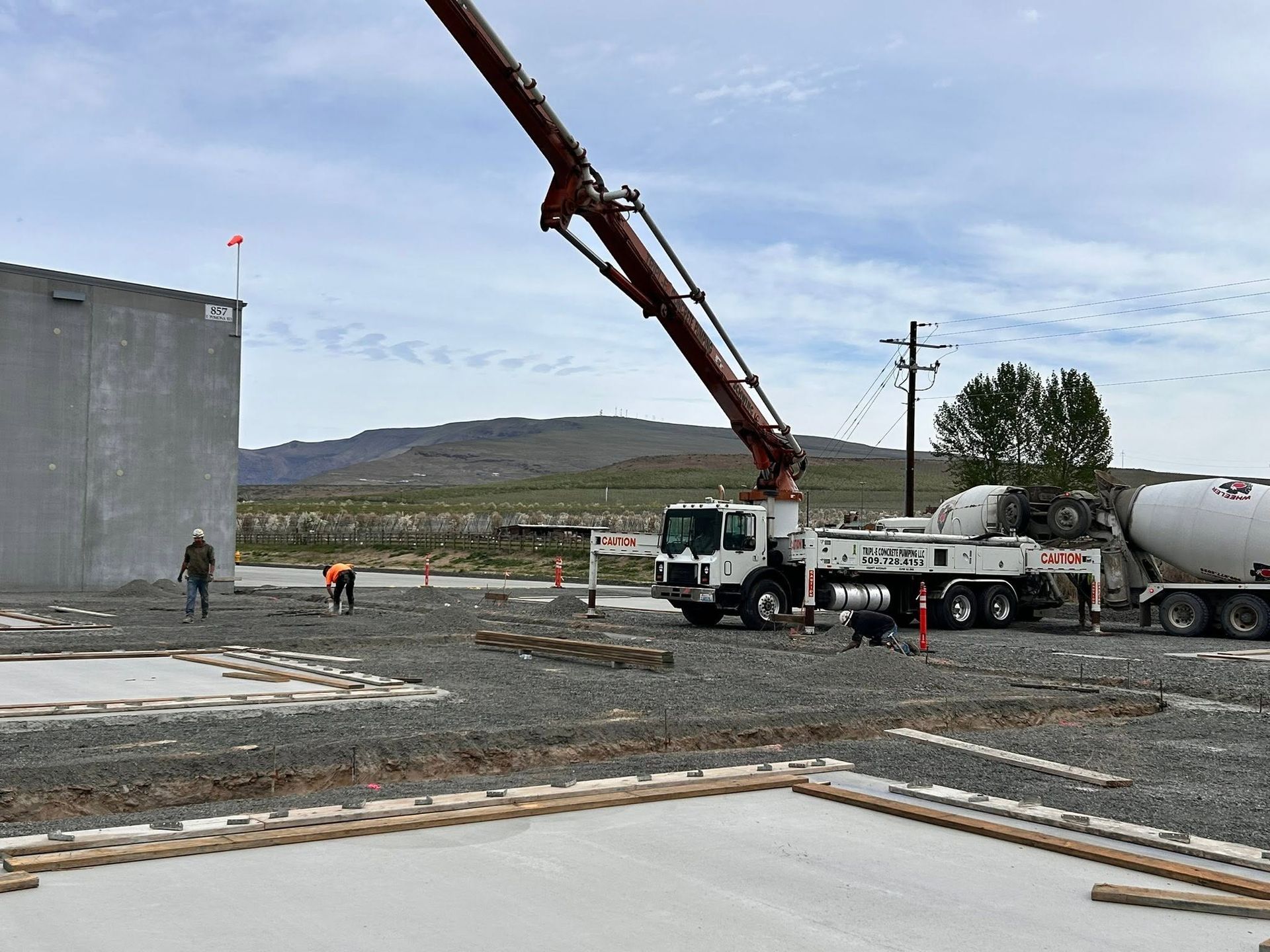Concrete pour at a construction site with a crane, cement truck, and workers near a large wall