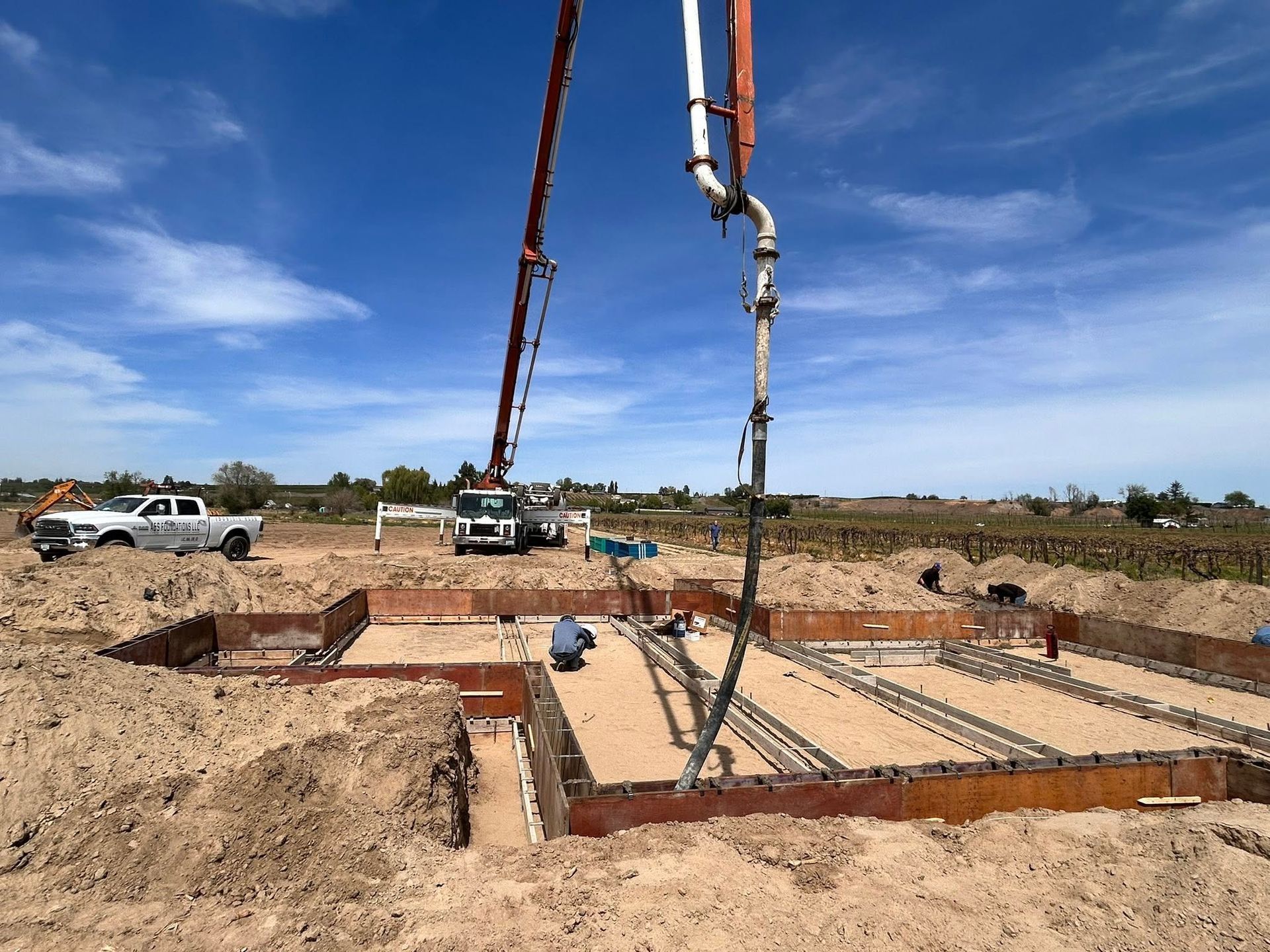 Concrete foundation poured on a construction site, with a concrete pump and trucks under a blue sky.