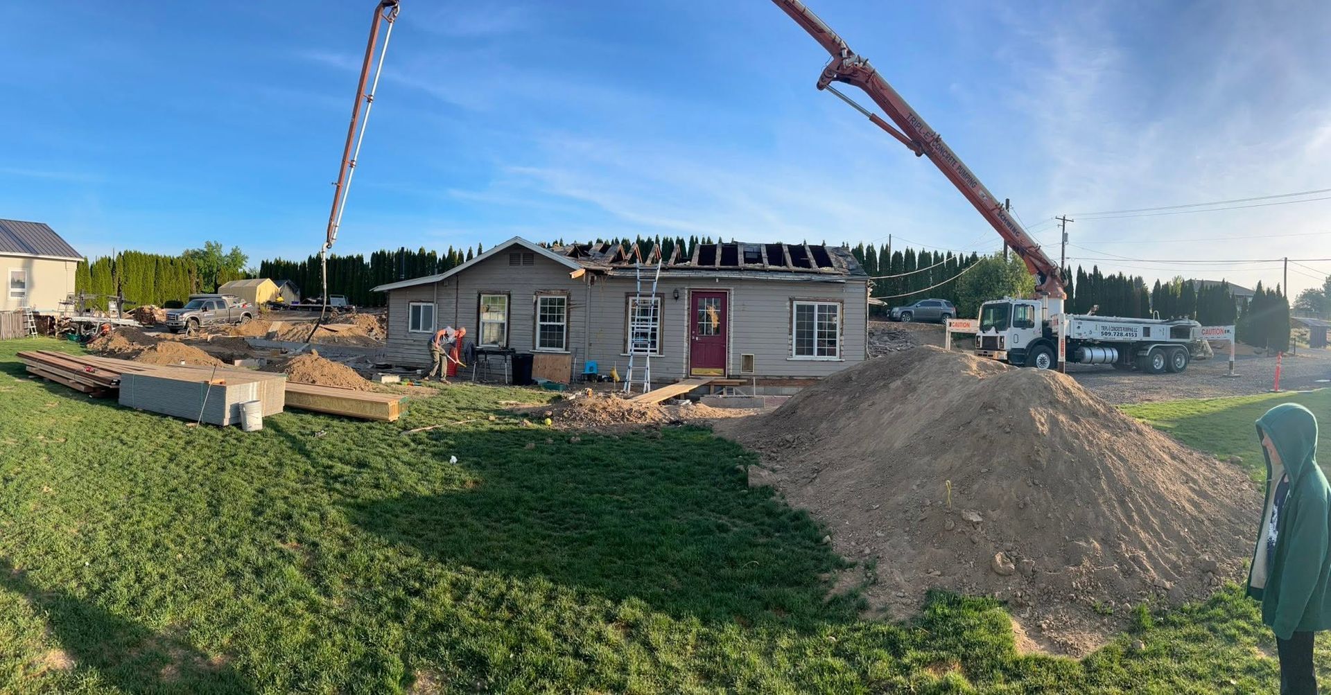 Construction site with a small house, concrete pumps, gravel pile, and workers under a clear sky