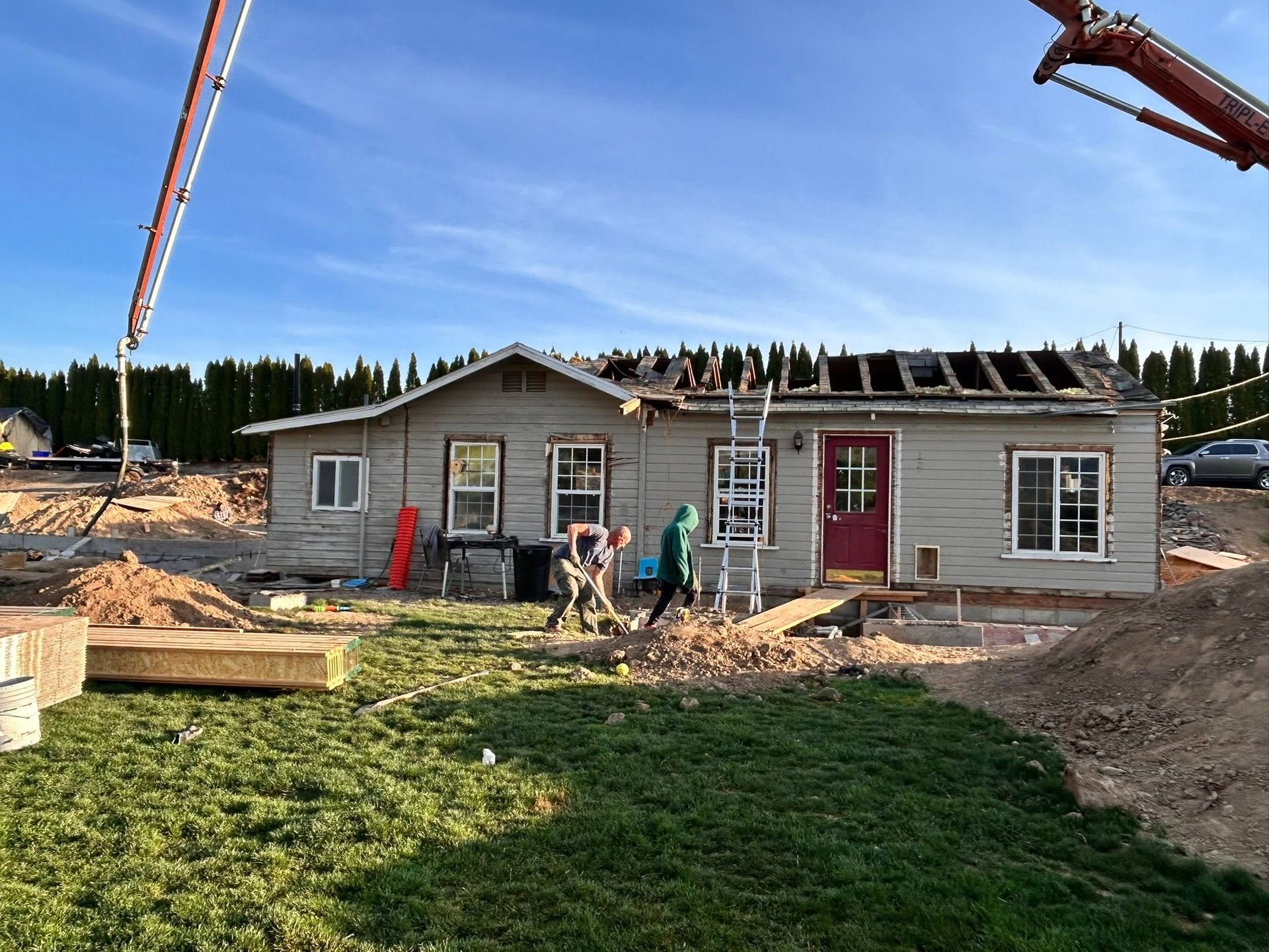 People working outside a house under construction with a crane and lumber nearby