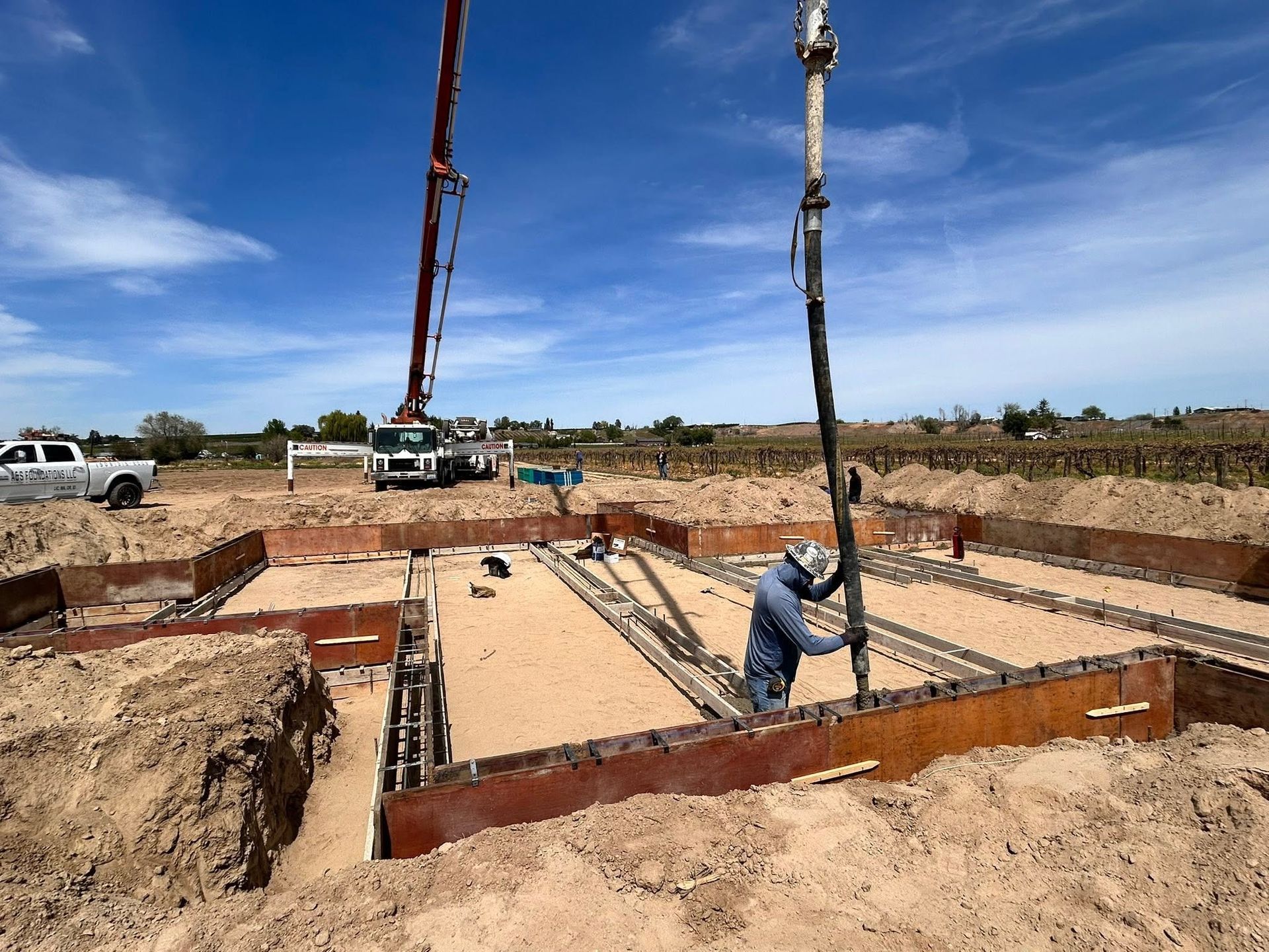 Construction site with concrete foundation forms, workers, and a concrete pump under a clear blue sky