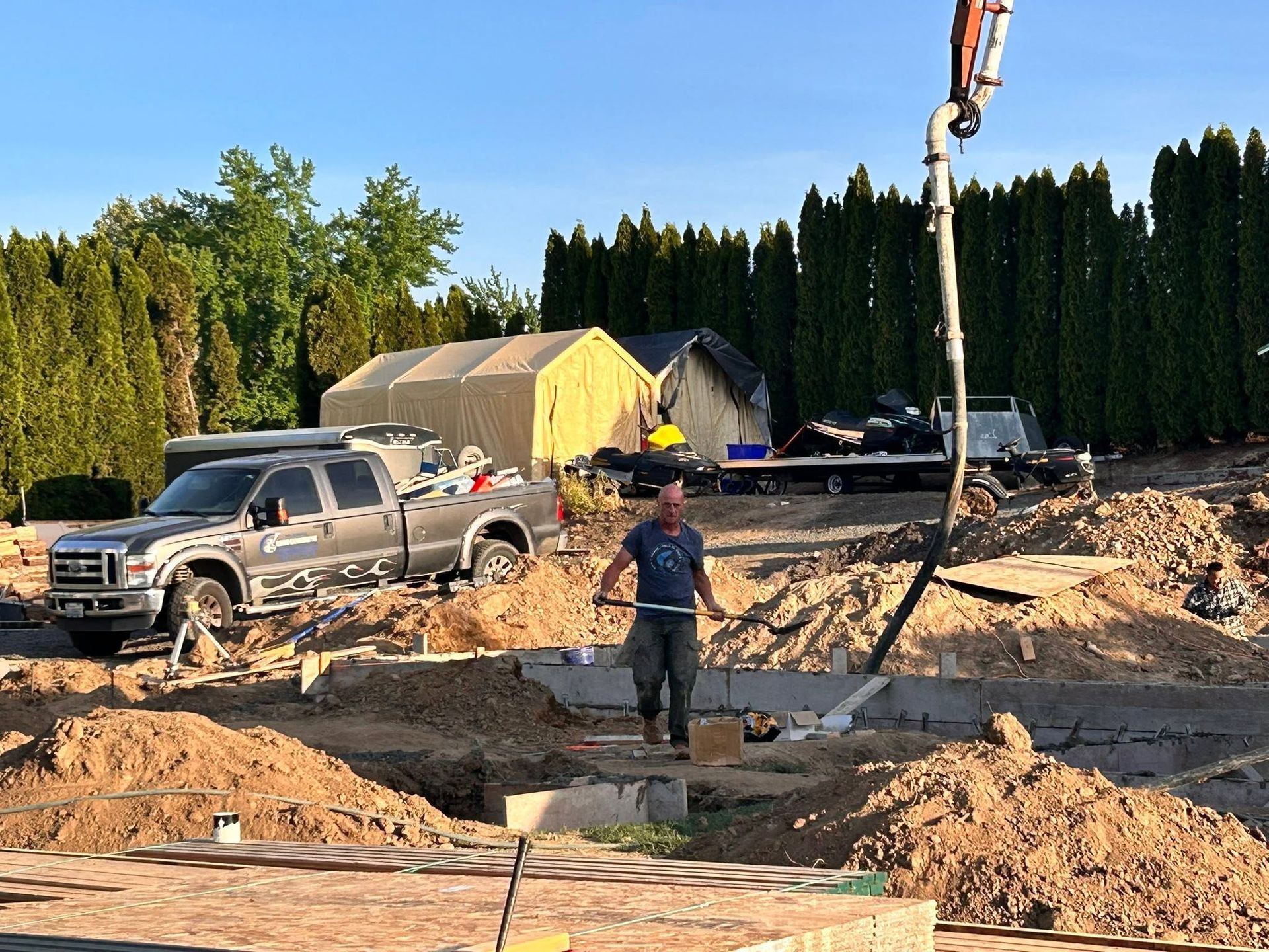 Construction site with excavator, pickup truck, worker, and a tent under a clear blue sky