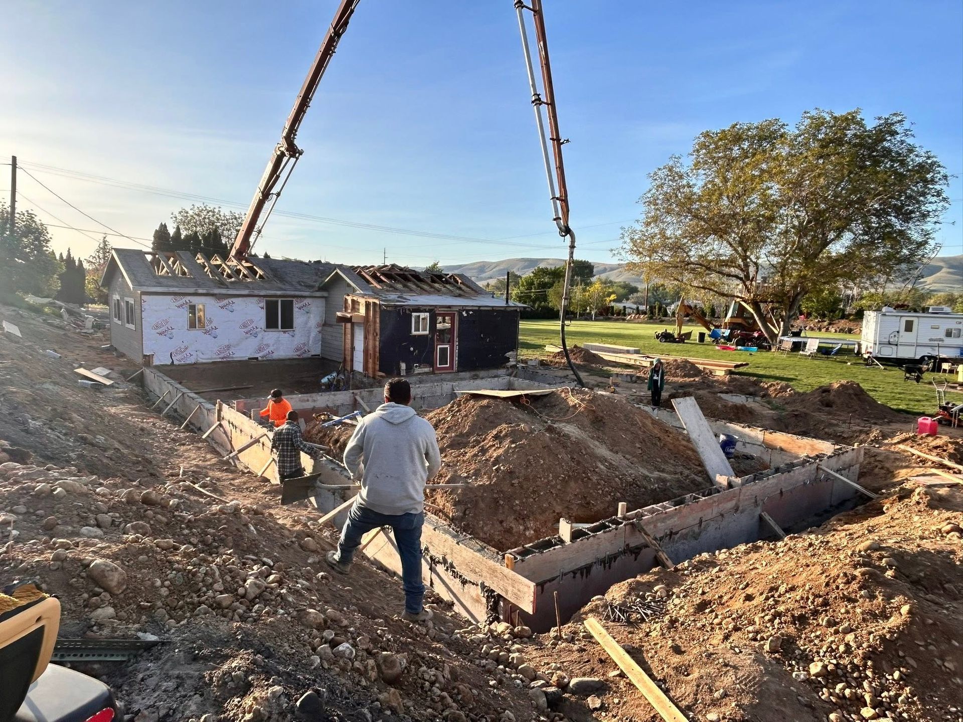 House being lowered into a foundation by crane on a construction site with two workers nearby