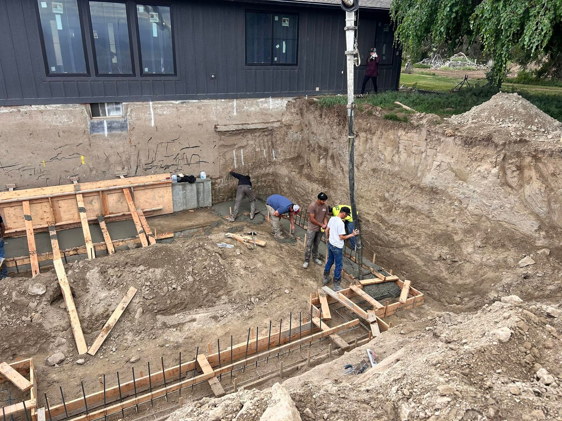 Workers at a house foundation excavation site with wooden formwork and dirt walls
