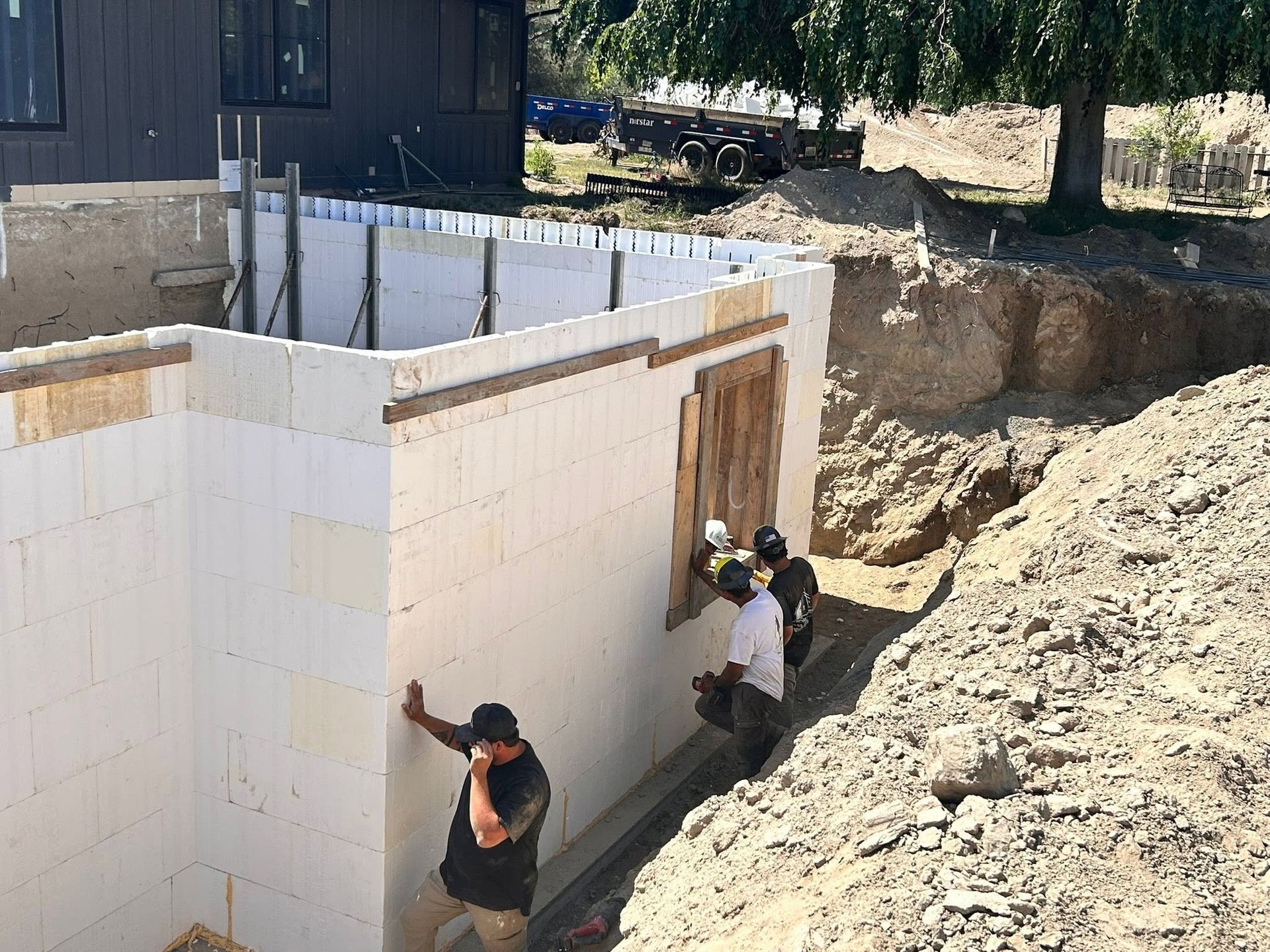 Workers install panels on an outdoor white building wall beside an excavated hillside.
