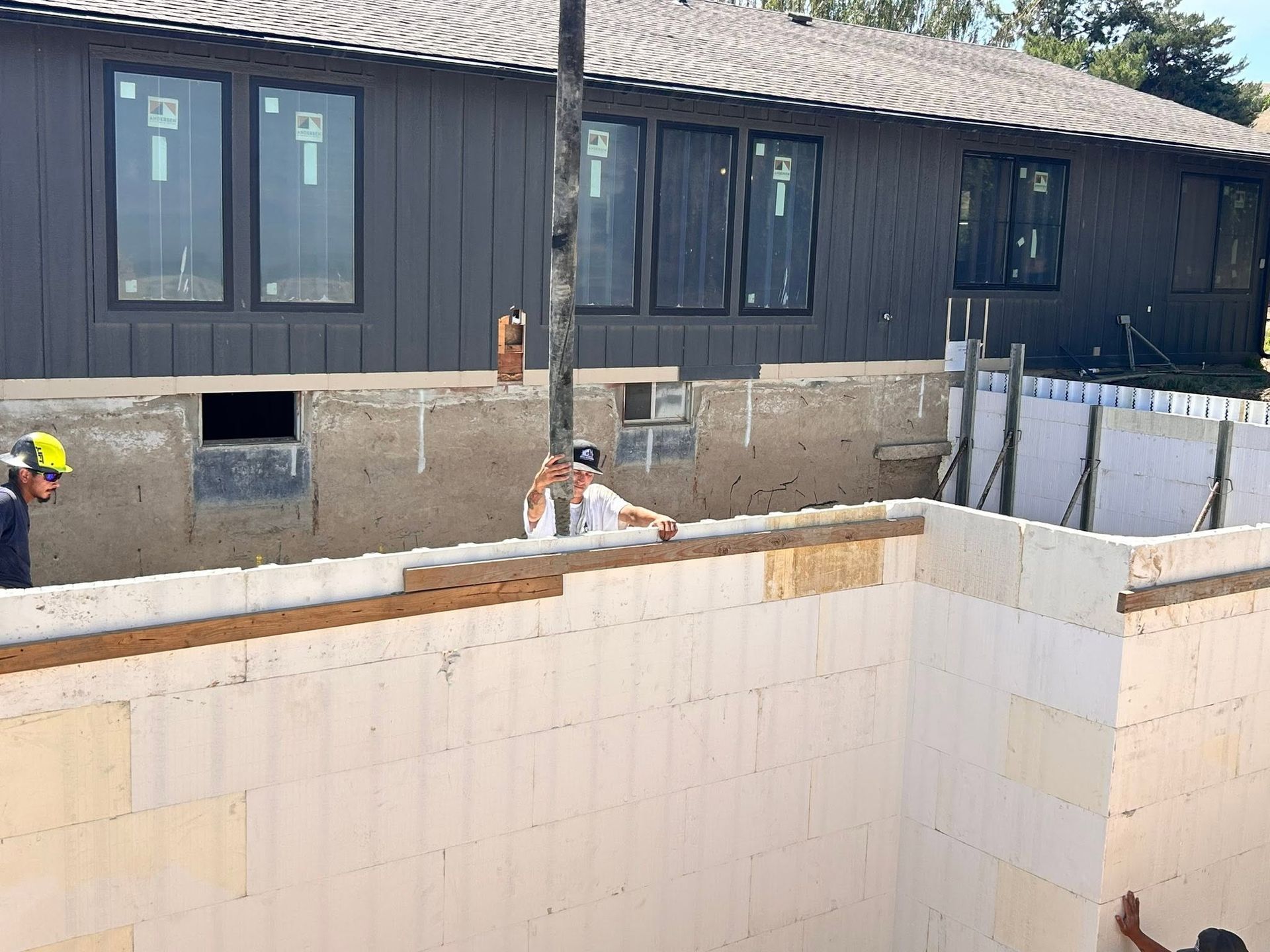 Construction site with workers beside a partially built white masonry wall and a dark building in the background