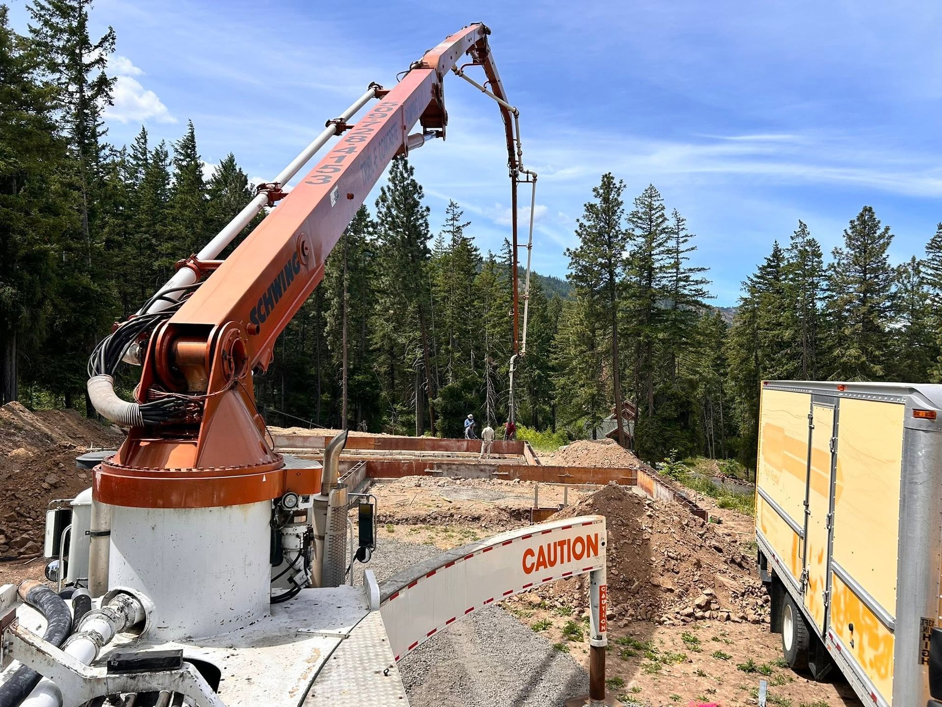 Crane lowering a cable at a construction site with trees and a caution barrier in the foreground