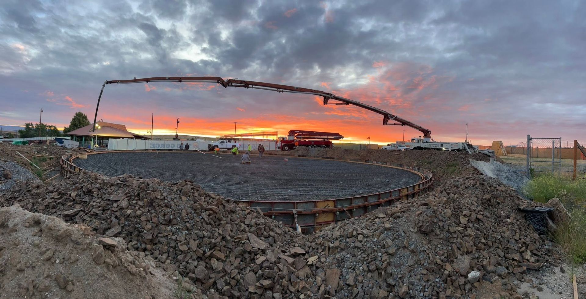 Concrete pump boom over a circular foundation at sunset on a construction site.