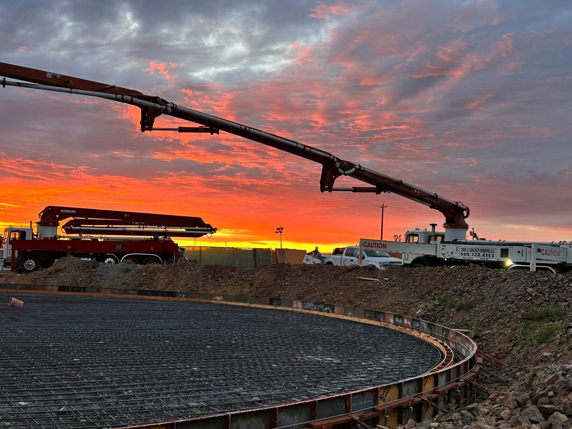 Concrete pump truck pouring at a construction site at sunset, with orange clouds and a circular foundation in the foreground