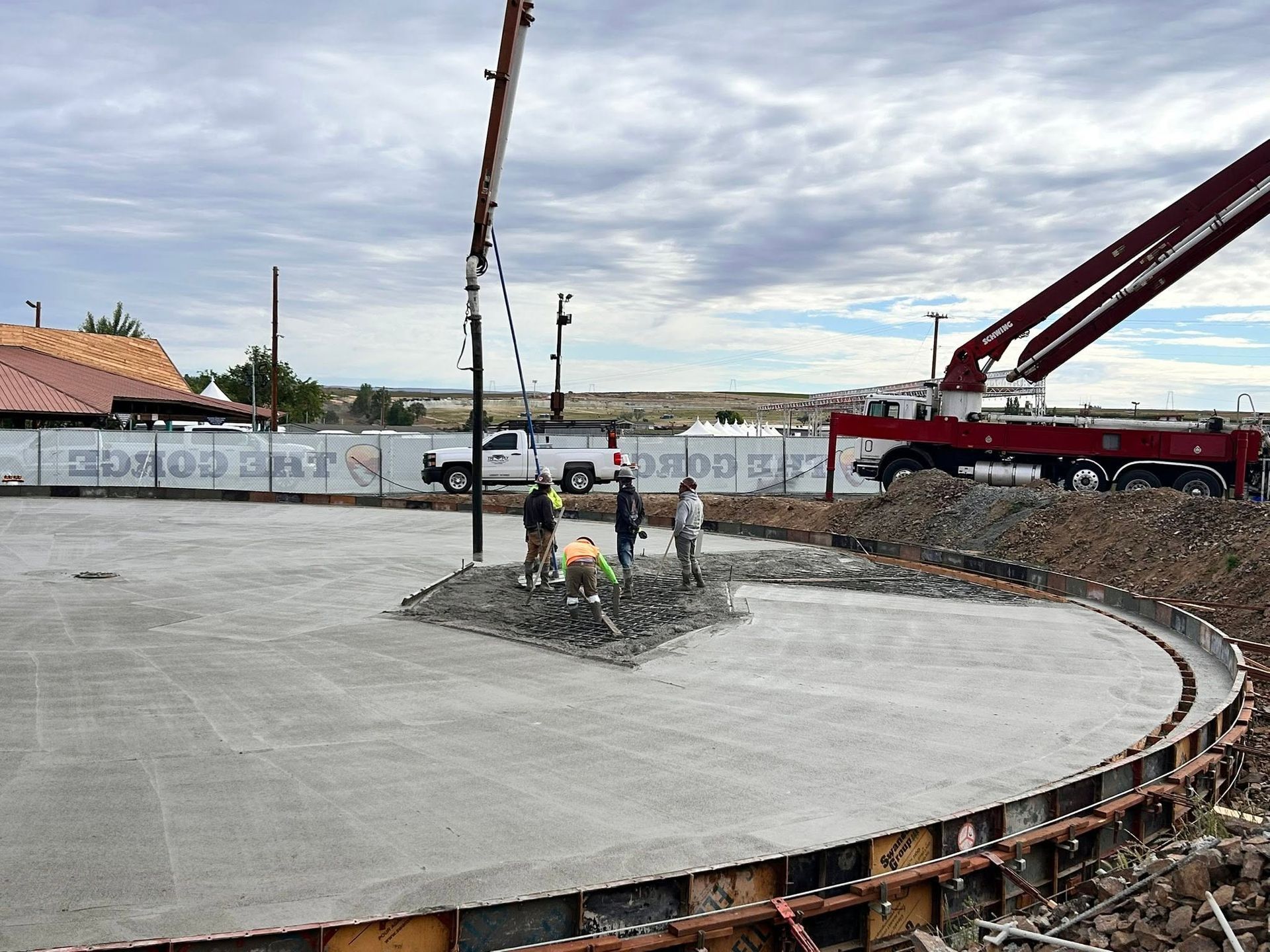 Concrete foundation under construction with workers, crane, and rebar on a cloudy site
