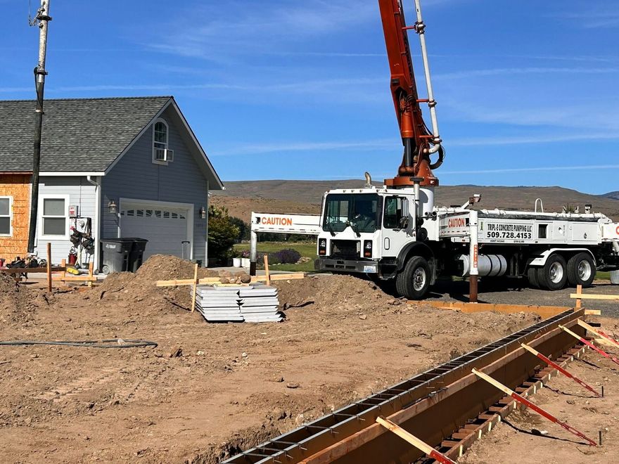 Concrete truck with boom pump at a construction site beside a house and foundation forms