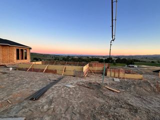 Partially built home at dusk with concrete foundation, dirt foreground, and city lights on the horizon