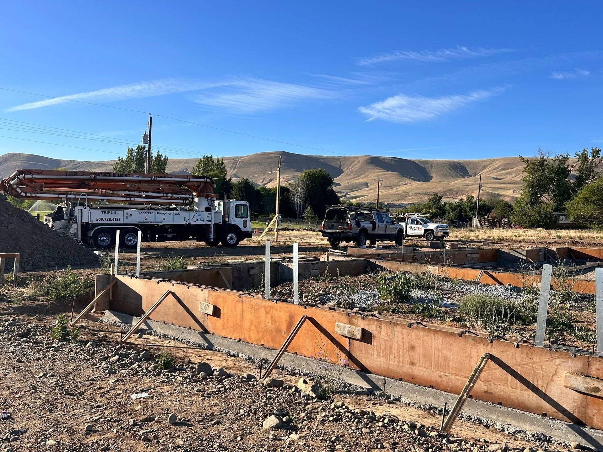 Construction site with trucks, orange barriers, and dry hills under a blue sky