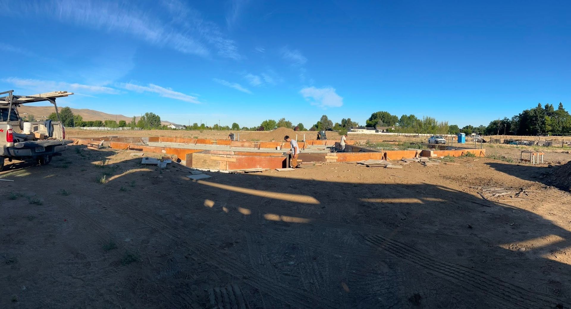 Construction site with excavators, dirt piles, and workers under a clear blue sky.