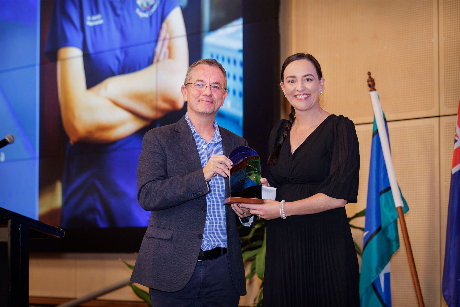 A women receiving an award on stage. Both people are looking at the camera smiling. 
