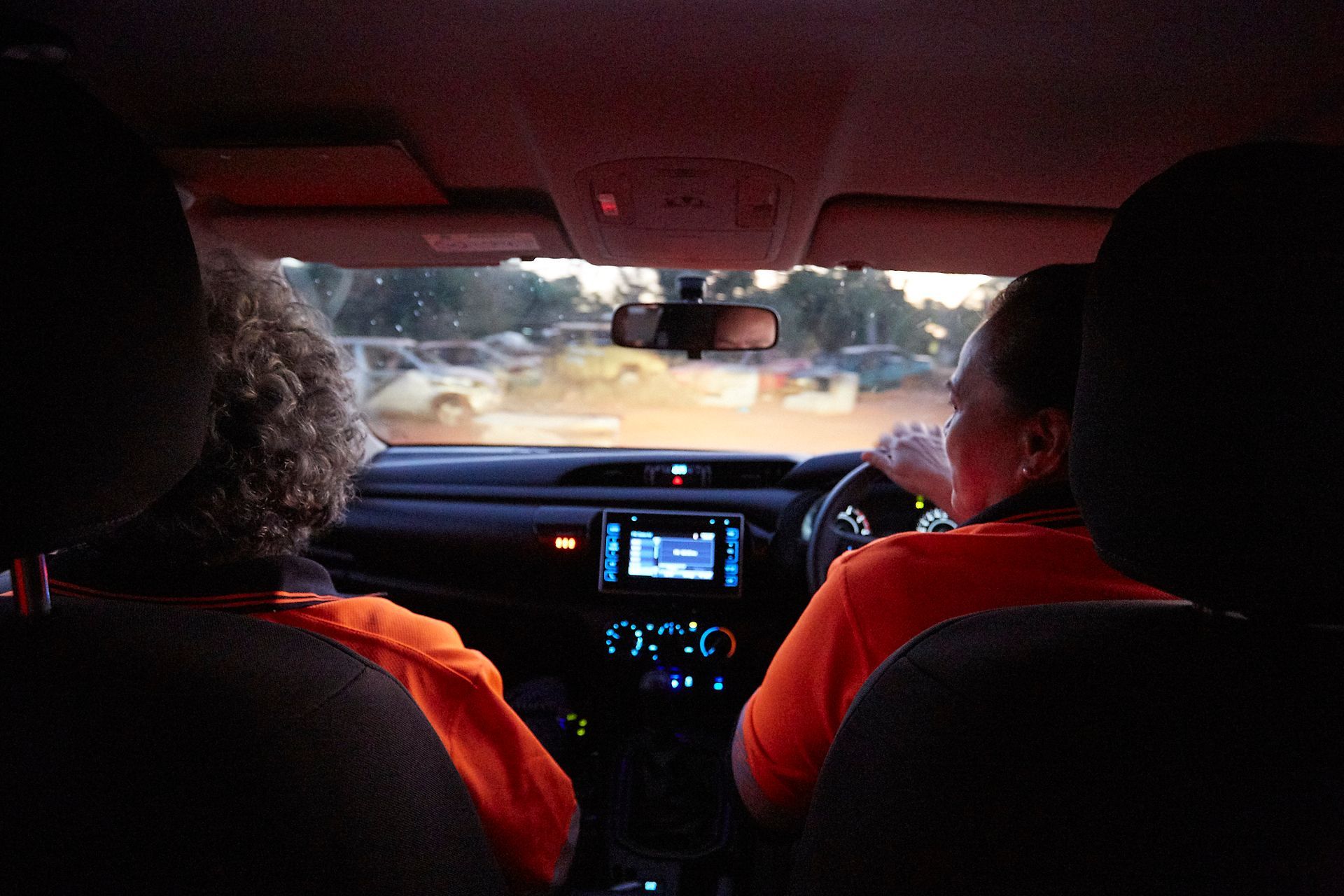 Two people wearing orange shirts in a car. 