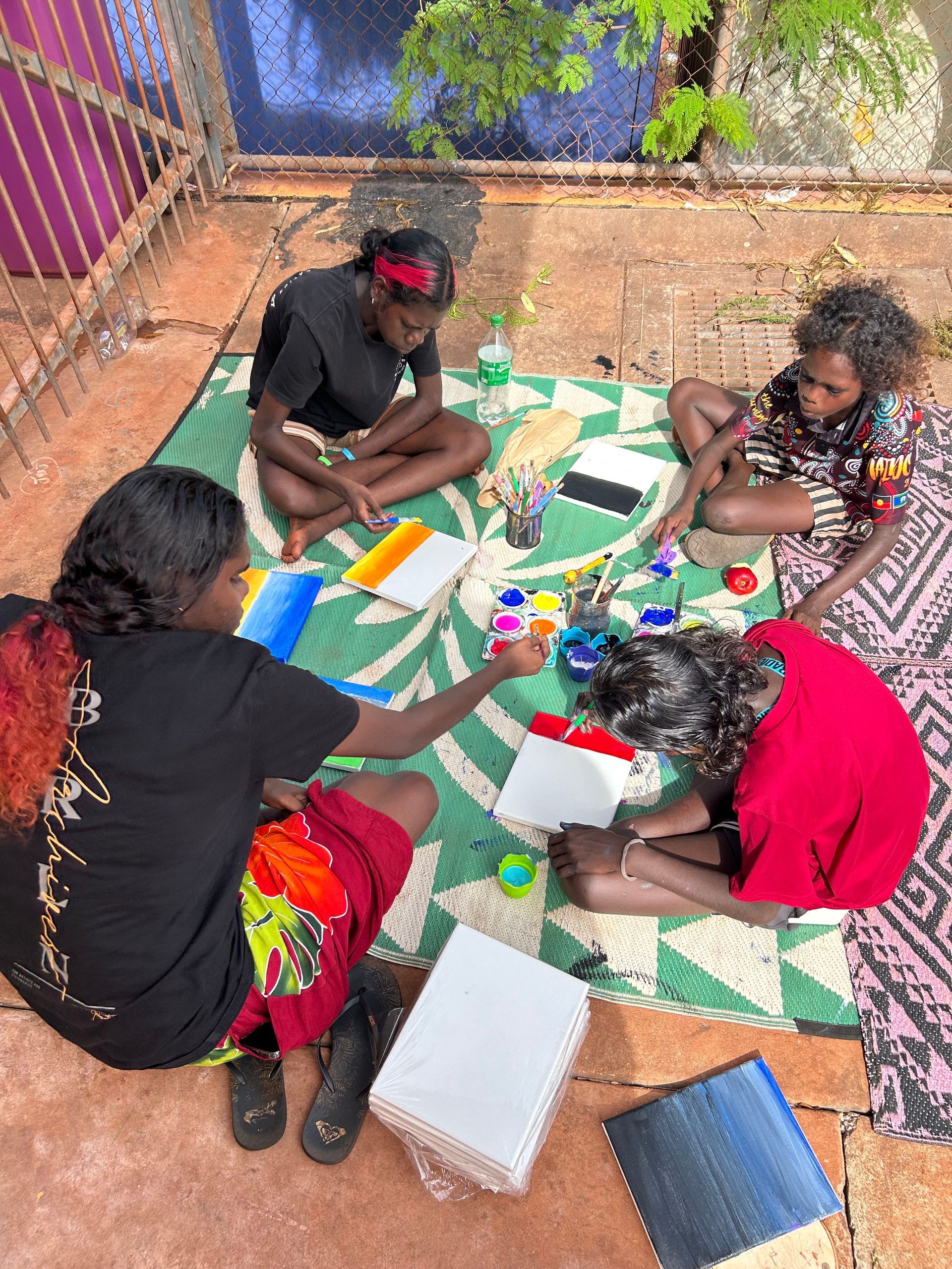Four people sit on a mat painting.