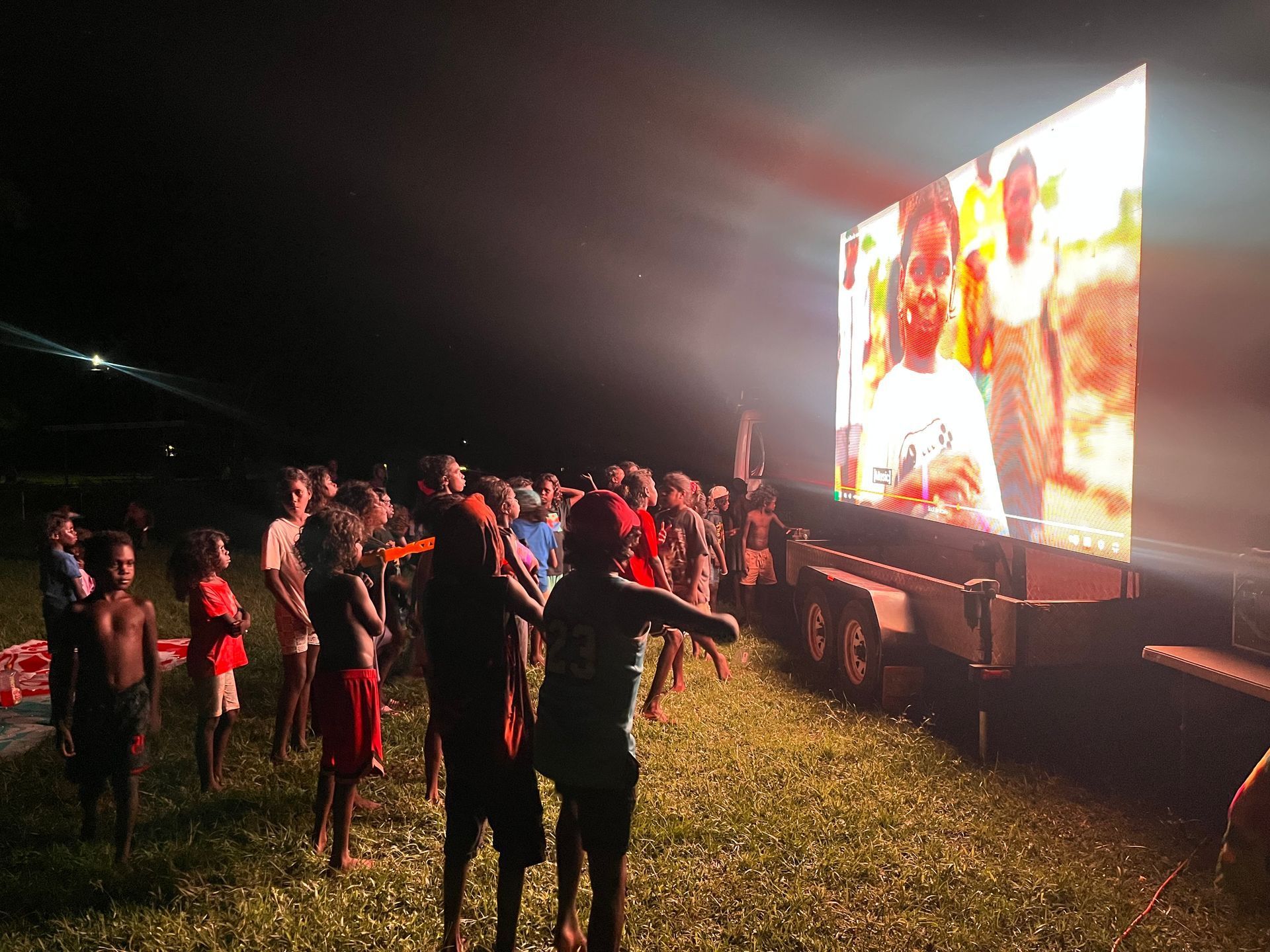 A group of kids watching a moving outdoors.
