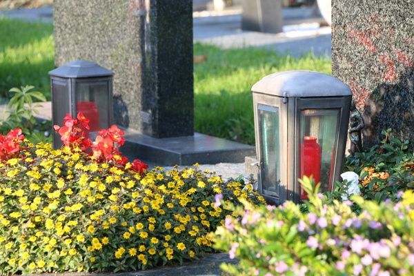 Flower bed with yellow and red blooms beside black lantern-style garden lights on a sunny lawn