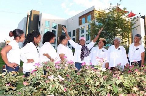 People in white coats standing outdoors in a garden, talking in front of a building.