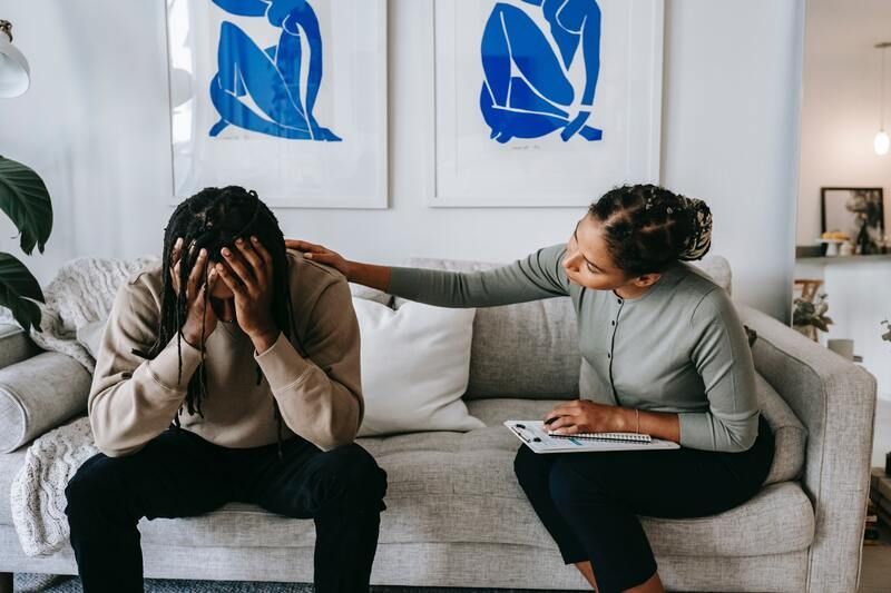 Therapist listening to a distressed client on a couch in a bright counseling office