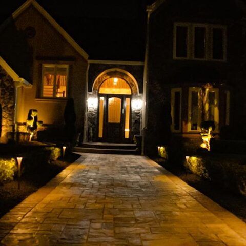 Illuminated brick walkway leading to a warmly lit house entrance at night