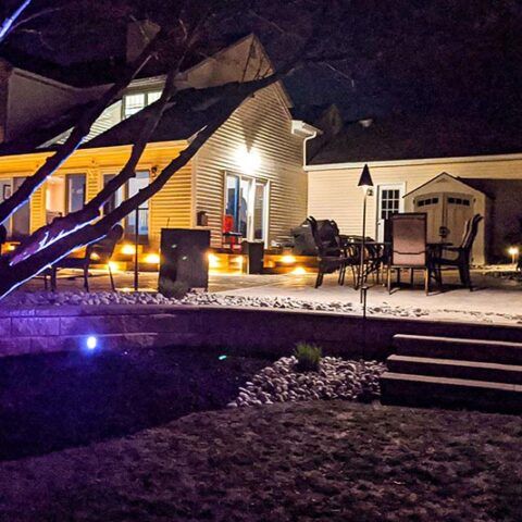 Backyard patio at night with string lights, chairs, and a house lit warmly in the background