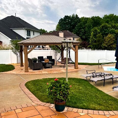 Backyard patio with gazebo seating, lounge chairs, and a swimming pool near a white fence