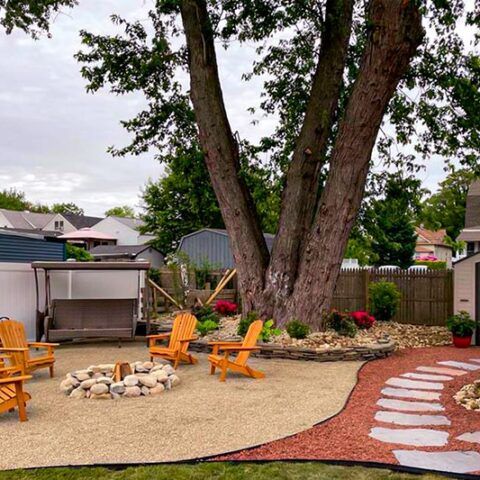 Backyard patio with fire pit, orange chairs, large tree, and stone stepping path