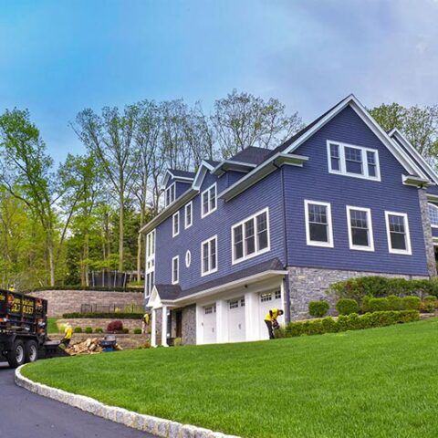 Blue-gray house with white trim and garage on a sloped green lawn