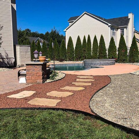 Backyard patio with curved stone path, pool, and tall hedges under a clear blue sky