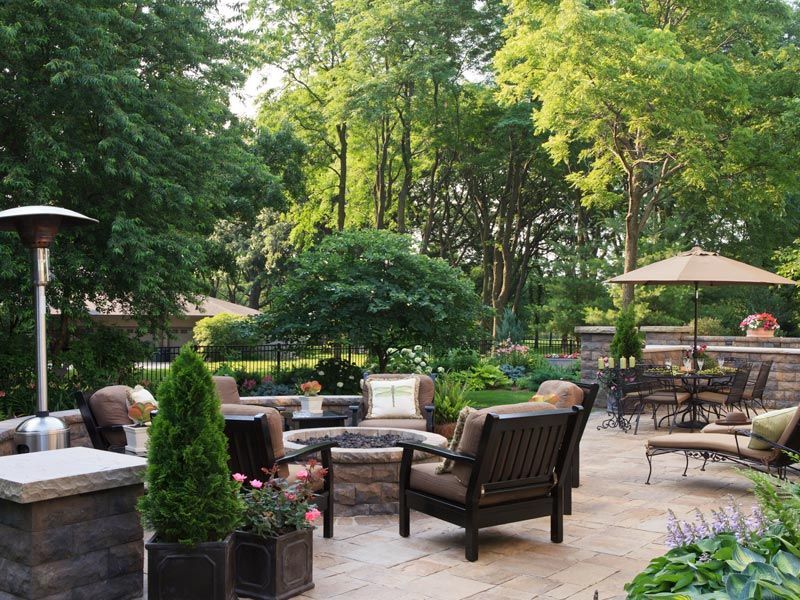 Patio seating area with wicker chairs, stone fire pit, and lush green garden surroundings